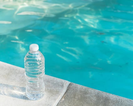 A plastic water bottle set on the edge of a swimming pool.
