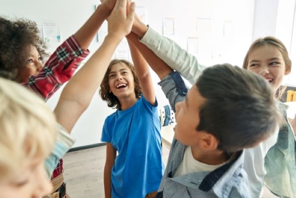 A group of 5 smiling kids put their hands together in a group high five.