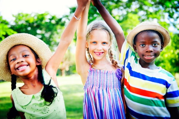 Three children standing together, holding hands high above their heads, showcasing a moment of joy and friendship.