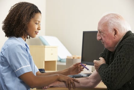 An elderly male gets a shot in his arm from a black, female nurse. 