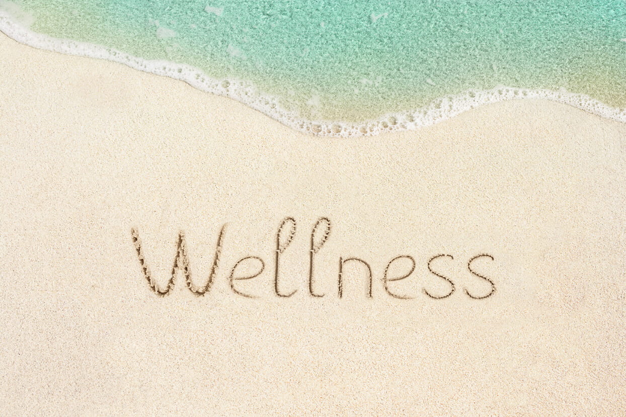 wellness word written in the sand on the beach.